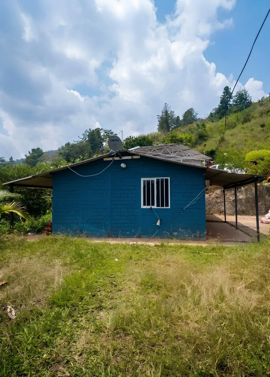 Casa 2, de fachada azul, sobre el prado y con la montaña al fondo