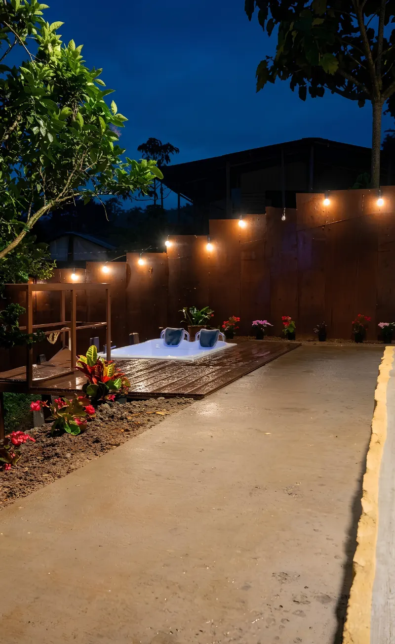 Jacuzzi al aire libre sobre deck de madera, entre muros de acero y luces colgantes